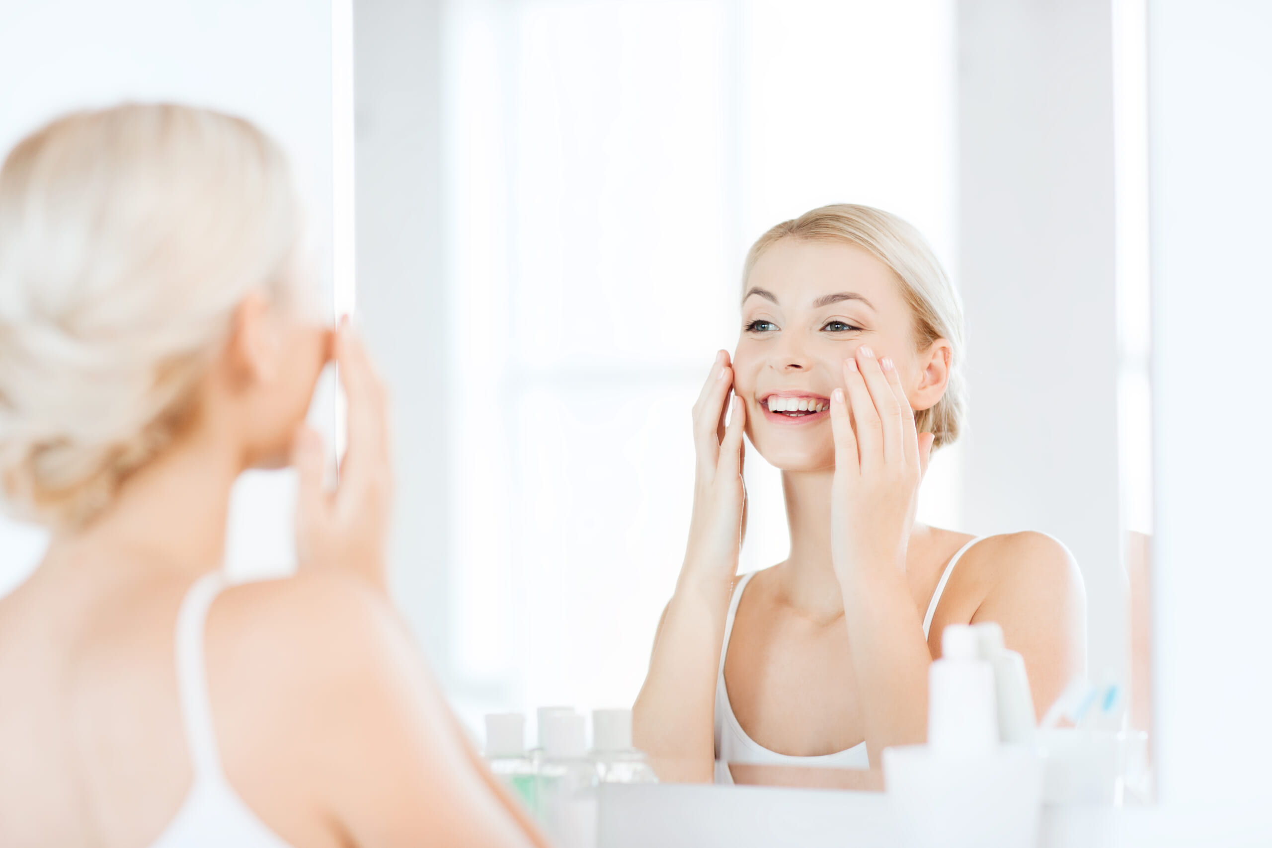 Smiling woman looking in the mirror after aesthetic treatment, enjoying healthy, radiant, and natural-looking skin
